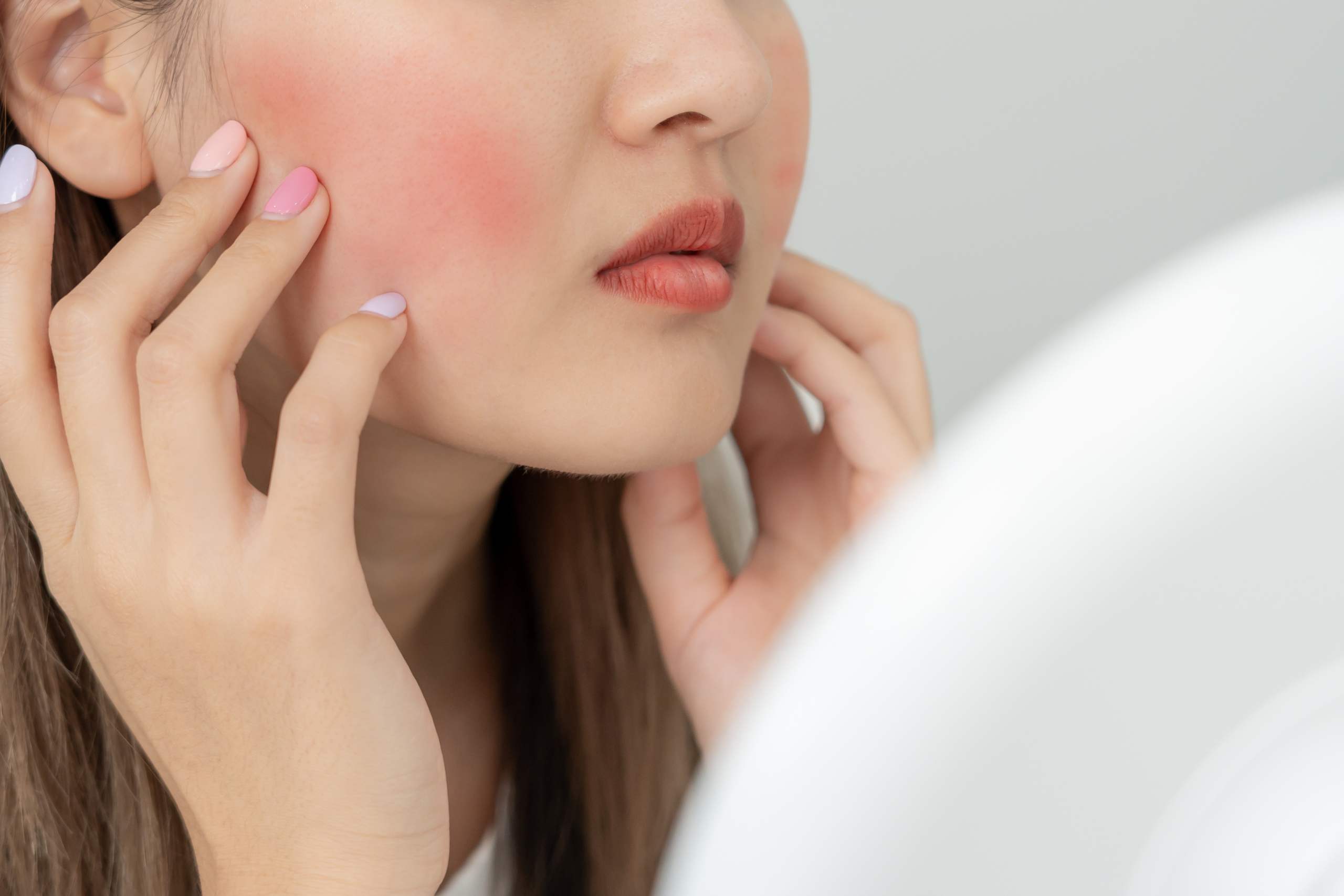 woman looking in the mirror wondering if her red nose from alcohol